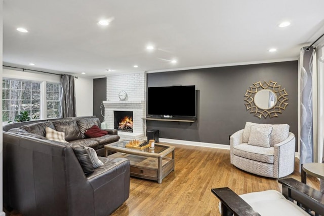 living room with a brick fireplace, ornamental molding, and light wood-type flooring