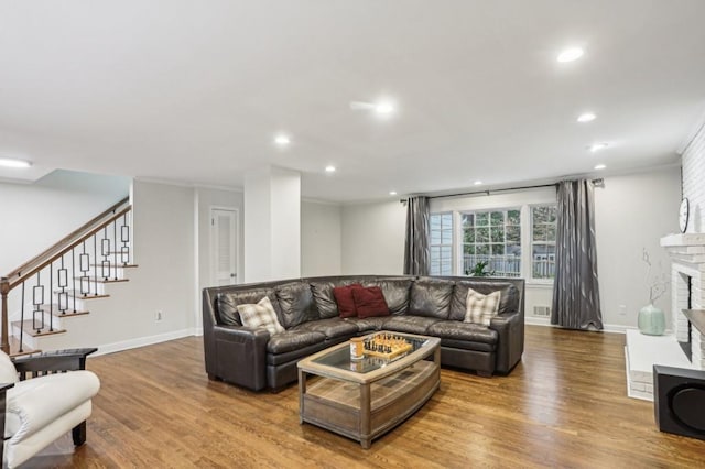 living room with hardwood / wood-style flooring, crown molding, and a brick fireplace