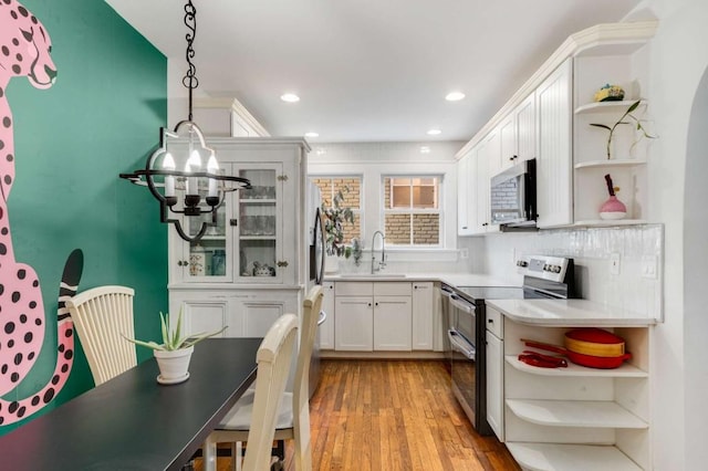 kitchen with sink, light hardwood / wood-style flooring, white cabinetry, hanging light fixtures, and stainless steel appliances