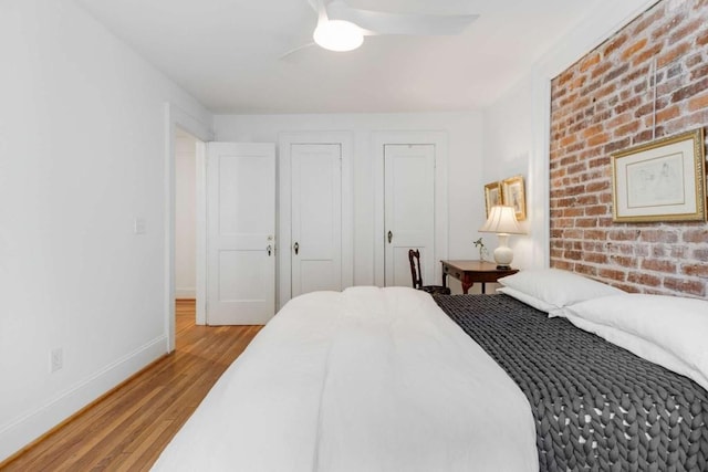 bedroom featuring ceiling fan, brick wall, and light hardwood / wood-style floors