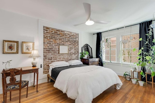 bedroom featuring hardwood / wood-style floors, ceiling fan, and brick wall