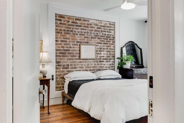 bedroom with hardwood / wood-style flooring, ceiling fan, and brick wall