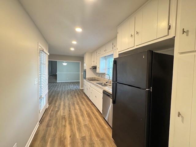 kitchen with a sink, stainless steel dishwasher, freestanding refrigerator, and white cabinetry