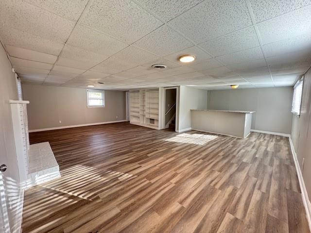 basement featuring visible vents, baseboards, a paneled ceiling, and wood finished floors