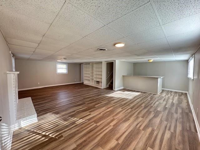 below grade area with visible vents, a paneled ceiling, baseboards, and wood finished floors