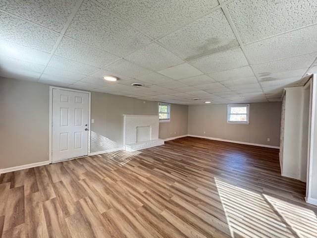 basement featuring a paneled ceiling, baseboards, and wood finished floors