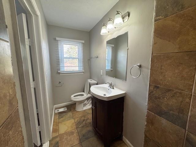 bathroom with toilet, vanity, baseboards, and visible vents