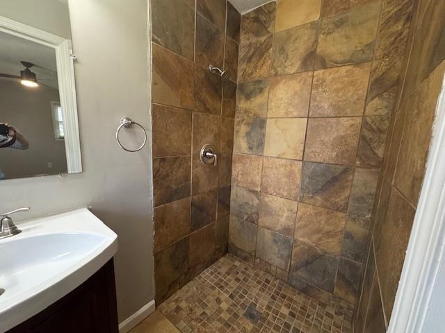 full bath with tiled shower, vanity, and a ceiling fan
