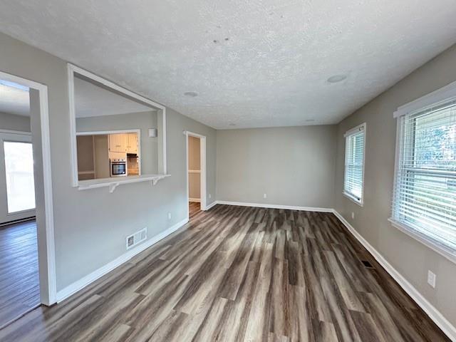 unfurnished living room featuring visible vents, baseboards, a textured ceiling, and dark wood finished floors