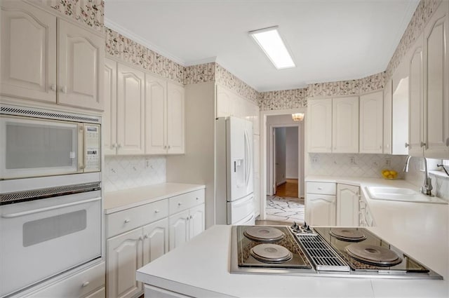 kitchen with white appliances, a sink, light countertops, backsplash, and crown molding