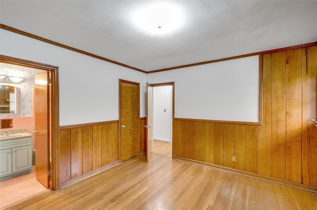 spare room featuring light wood finished floors, wooden walls, a sink, and wainscoting