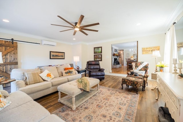 living room featuring wood-type flooring, ornamental molding, a wall unit AC, ceiling fan, and a barn door