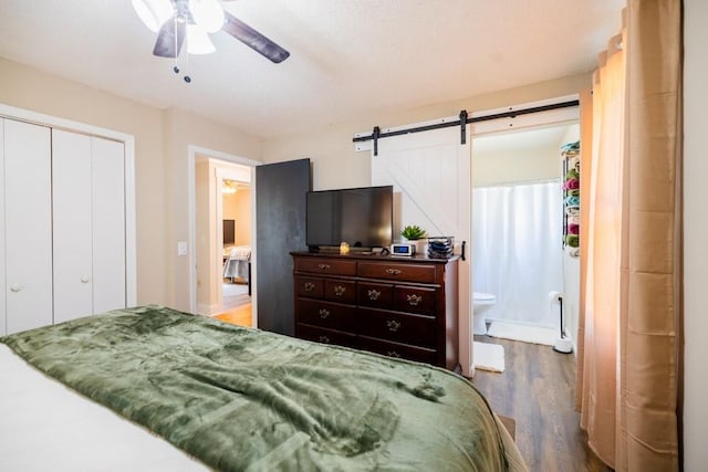 bedroom with wood-type flooring, a barn door, ceiling fan, and a closet