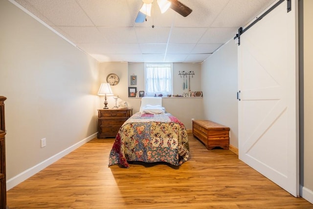 bedroom with ceiling fan, a barn door, light wood-type flooring, and a drop ceiling