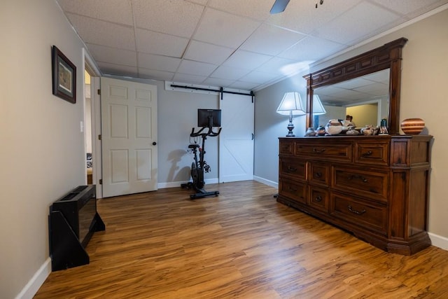 exercise area featuring wood-type flooring, a barn door, ceiling fan, and a paneled ceiling