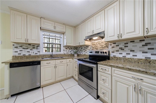 kitchen with sink, light tile patterned floors, appliances with stainless steel finishes, light stone countertops, and backsplash