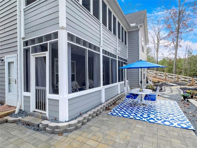 view of home's exterior with a patio, a shingled roof, fence, and a sunroom