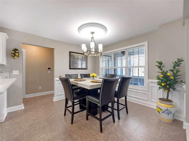 dining space featuring light tile patterned flooring, a decorative wall, a wainscoted wall, a notable chandelier, and baseboards