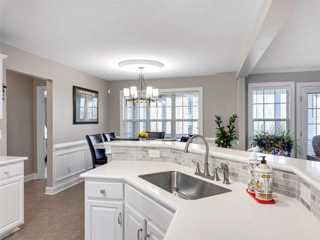 kitchen with light countertops, a sink, a notable chandelier, and white cabinetry