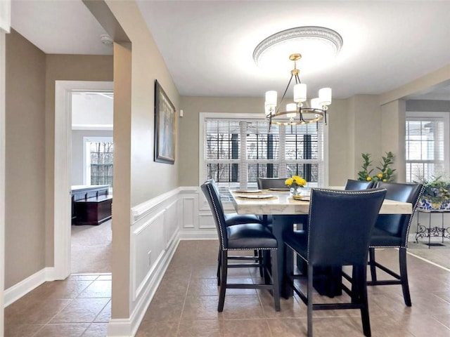 tiled dining room with a decorative wall, a notable chandelier, and wainscoting