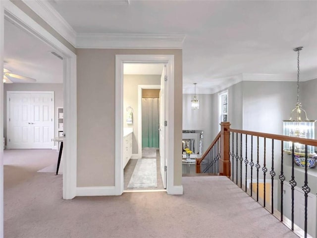 hall with carpet floors, crown molding, an upstairs landing, and an inviting chandelier