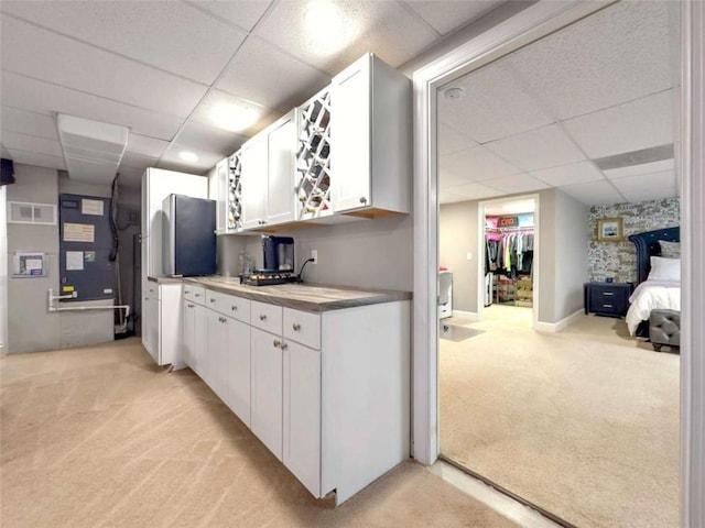 kitchen featuring a paneled ceiling, light colored carpet, visible vents, and white cabinetry