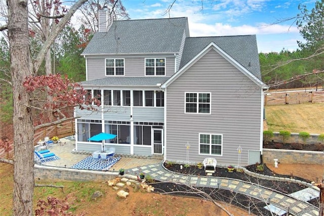 rear view of property featuring a patio, a shingled roof, a chimney, and a sunroom