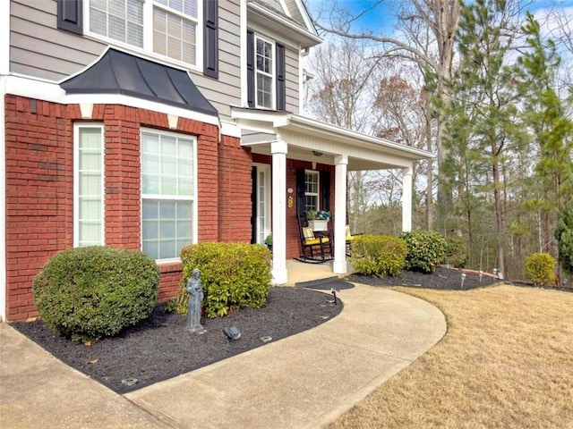 doorway to property with covered porch, metal roof, brick siding, and a standing seam roof