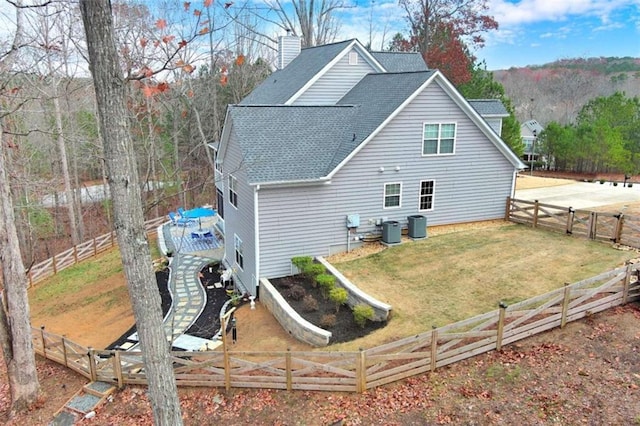 back of property featuring a lawn, a fenced backyard, a chimney, a wooden deck, and central AC