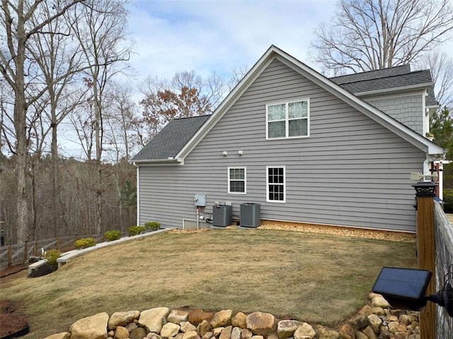 rear view of house with fence, central AC unit, and a yard