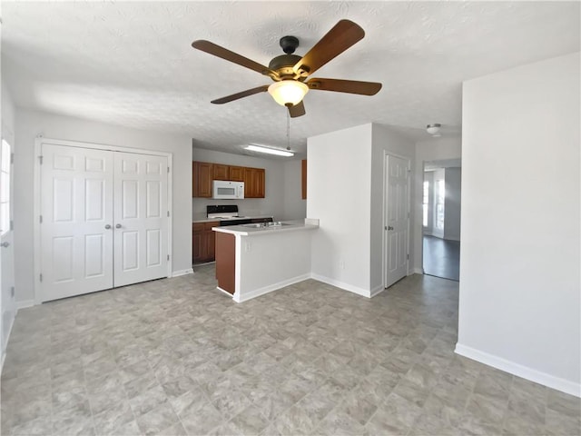 kitchen with white microwave, a peninsula, electric range, light countertops, and brown cabinets
