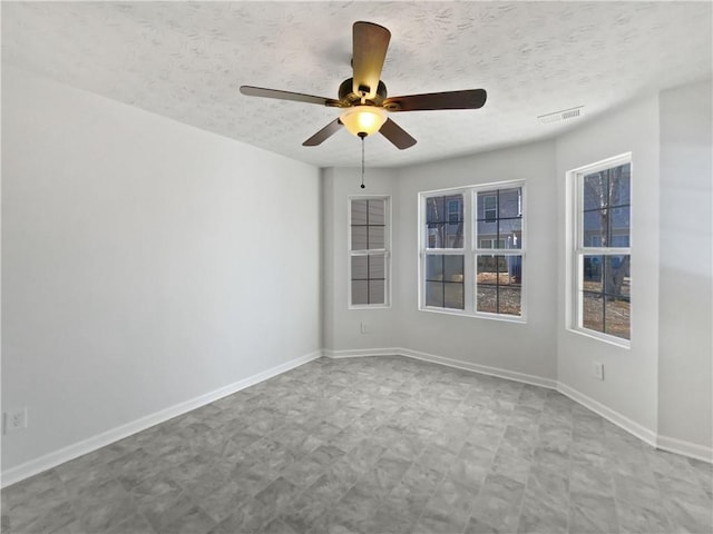 empty room with a textured ceiling, a ceiling fan, visible vents, baseboards, and tile patterned floors