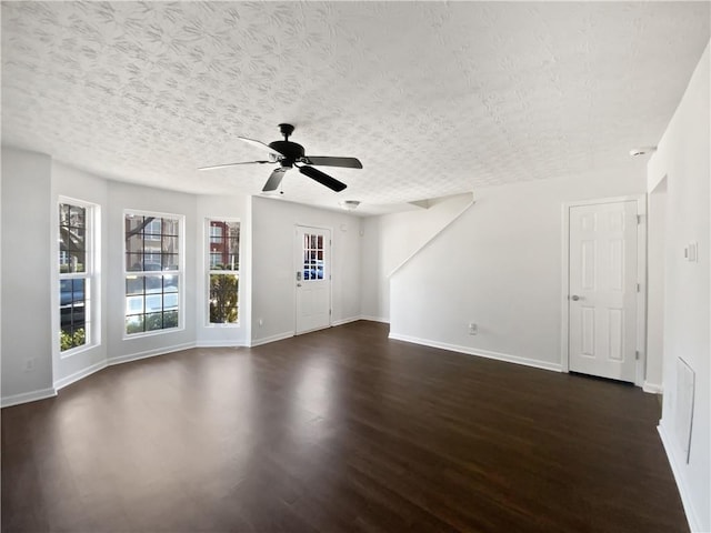 unfurnished living room with a ceiling fan, a textured ceiling, baseboards, and dark wood-style flooring