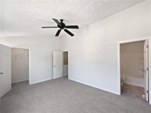 unfurnished bedroom featuring baseboards, connected bathroom, a spacious closet, vaulted ceiling, and carpet flooring