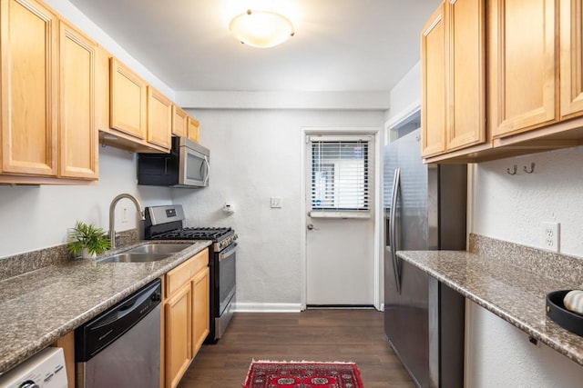 kitchen with appliances with stainless steel finishes, light brown cabinetry, sink, dark stone countertops, and dark hardwood / wood-style flooring