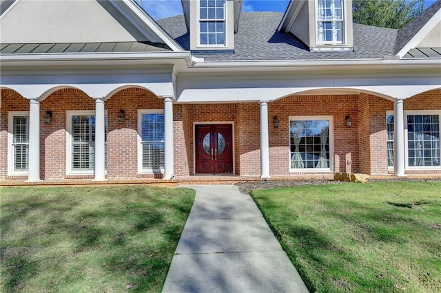 doorway to property with metal roof, a standing seam roof, a yard, a porch, and brick siding