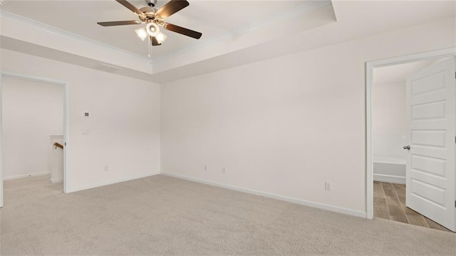 unfurnished bedroom with a raised ceiling, light carpet, ceiling fan, and baseboards