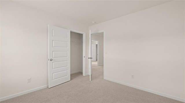 unfurnished bedroom with a closet, light colored carpet, and baseboards