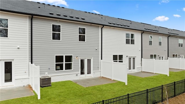 rear view of house with a patio, central AC unit, fence private yard, a lawn, and roof with shingles