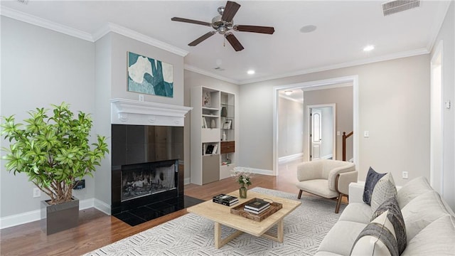 living room featuring wood-type flooring, crown molding, ceiling fan, and a fireplace