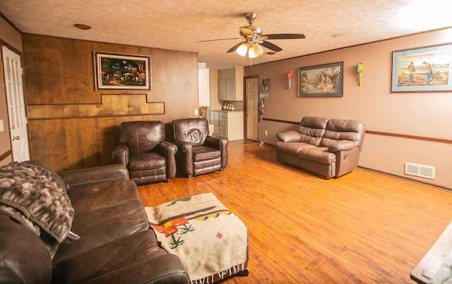 living room with ceiling fan, hardwood / wood-style flooring, wood walls, and a textured ceiling