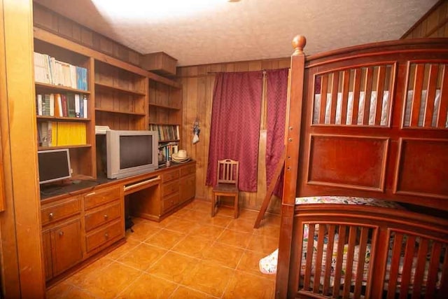 bedroom featuring light tile patterned flooring, built in desk, wood walls, and a textured ceiling