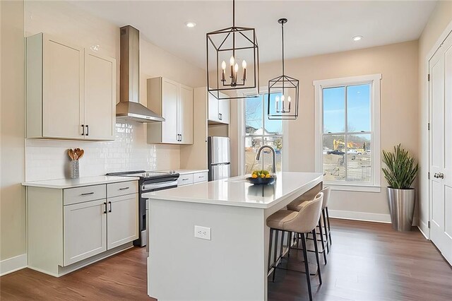 kitchen with sink, appliances with stainless steel finishes, white cabinets, a center island with sink, and wall chimney exhaust hood