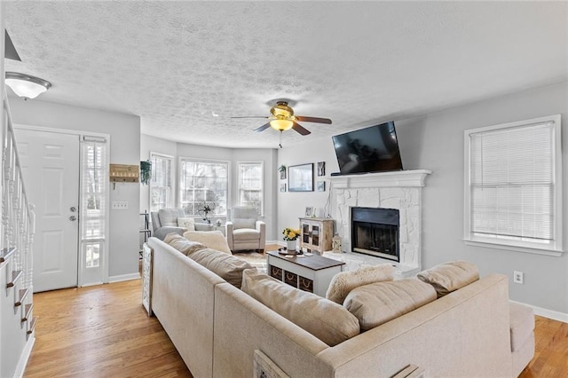 living room with a textured ceiling, a stone fireplace, light wood-style flooring, baseboards, and stairway