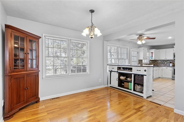 kitchen with light wood-type flooring, tasteful backsplash, visible vents, and stainless steel stove