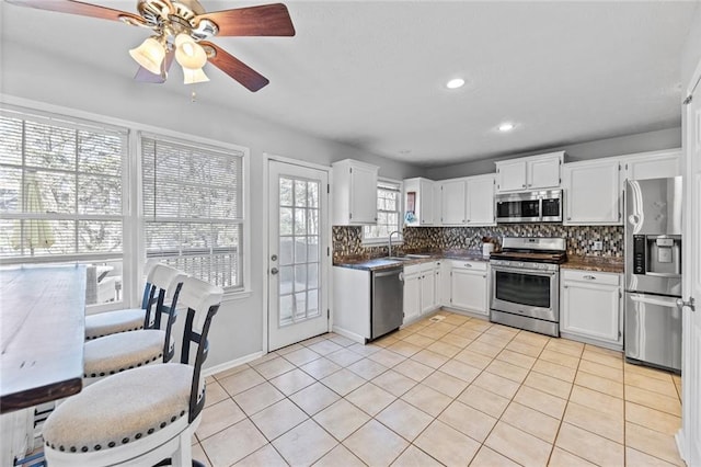 kitchen featuring dark countertops, decorative backsplash, appliances with stainless steel finishes, white cabinets, and light tile patterned flooring