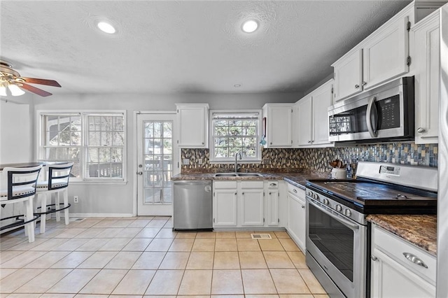 kitchen featuring tasteful backsplash, white cabinets, appliances with stainless steel finishes, a sink, and light tile patterned flooring