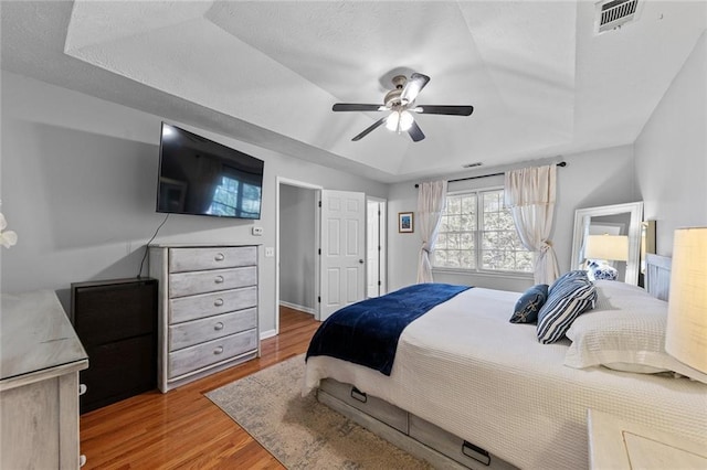 bedroom with baseboards, visible vents, a raised ceiling, ceiling fan, and wood finished floors