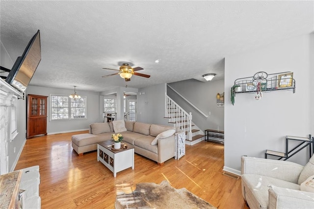 living room with light wood finished floors, stairway, a textured ceiling, baseboards, and ceiling fan with notable chandelier