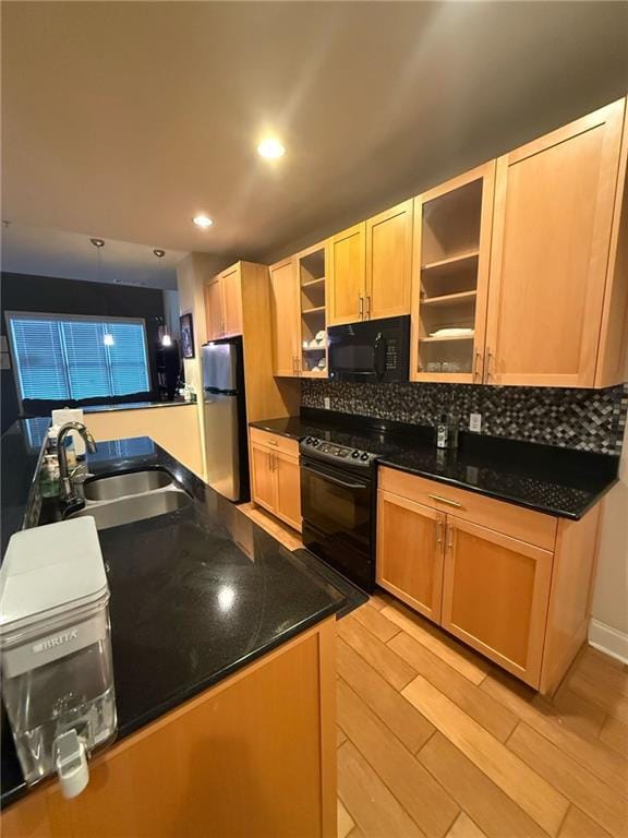 kitchen with sink, tasteful backsplash, dark stone countertops, light hardwood / wood-style floors, and black appliances